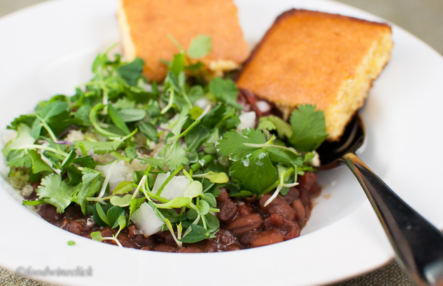 Top the chili with onions, shredded cheese, and a mix of cilantro and micro-greens